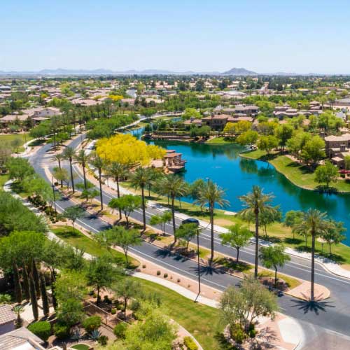 Aerial view of a suburban neighborhood in Chandler Arizona with a lake, roads, and neatly arranged houses.
