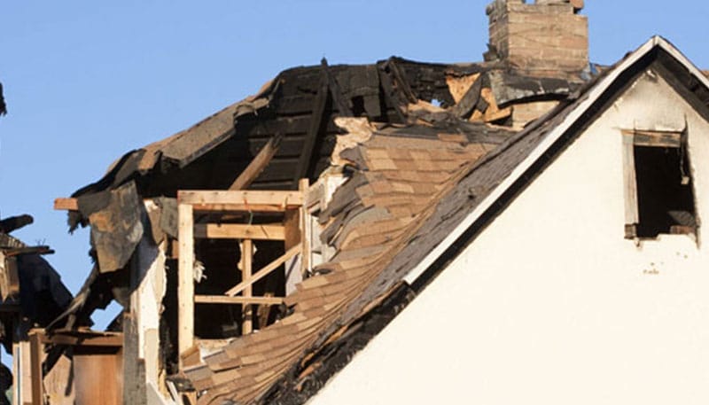 Partially collapsed roof of a damaged house with exposed wooden beams.