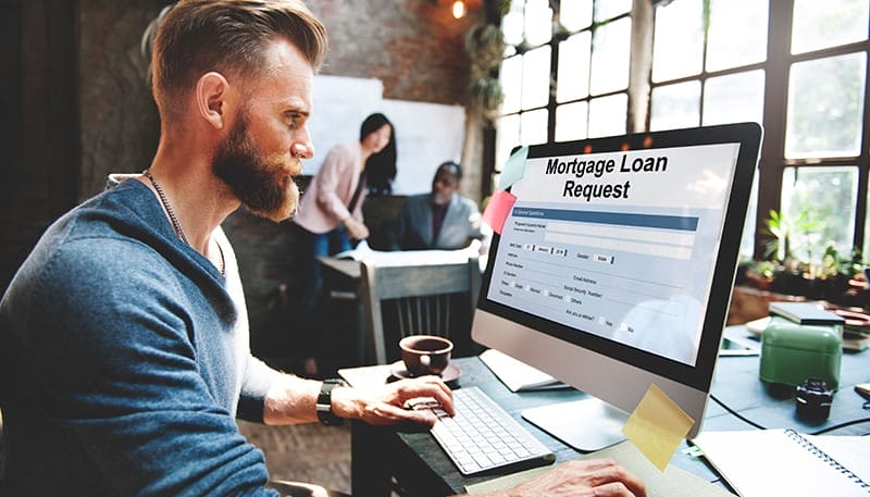 Man filling out a mortgage loan request on a computer in a modern office setting.