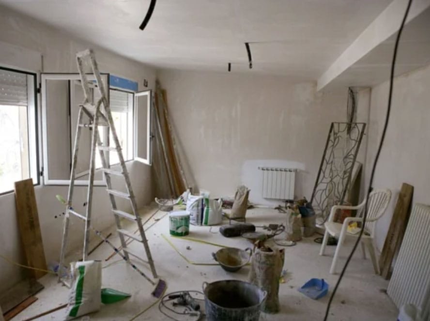 Room under renovation with ladder, paint buckets, and construction materials scattered around.