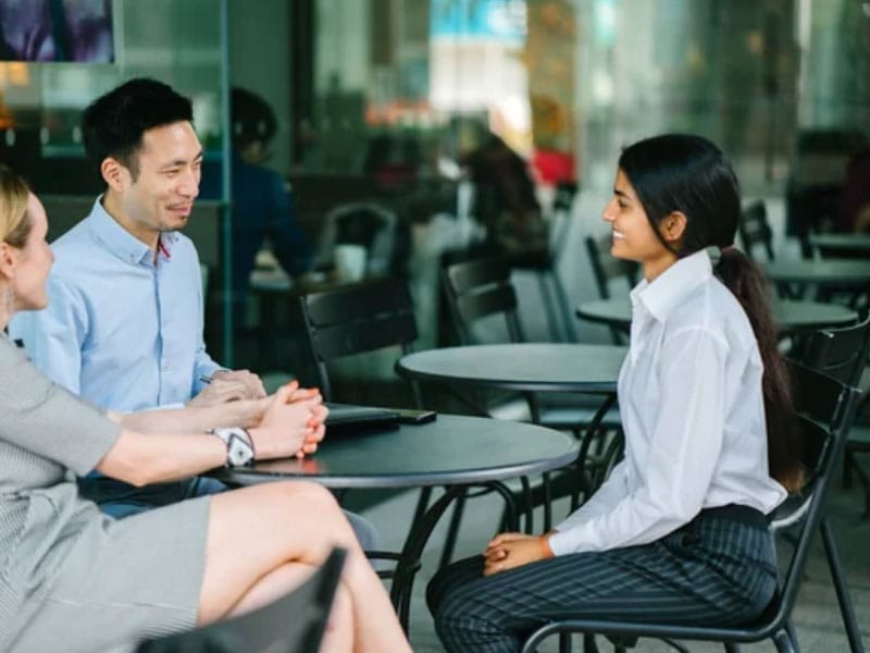 Three professionals engaged in a conversation at a cafe.