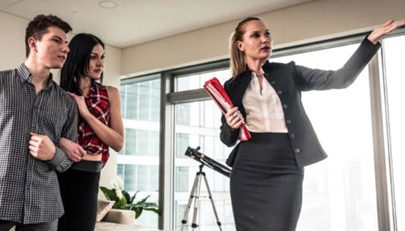 Business presentation: a woman gestures towards a window while addressing two attentive colleagues in an office setting.