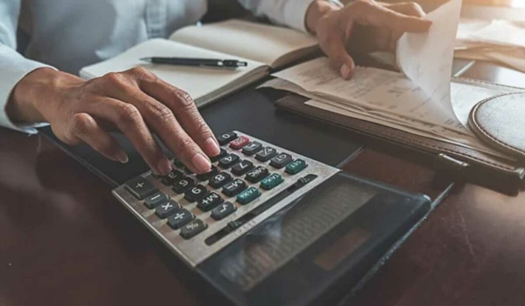 Person using a calculator and organizing receipts at a desk, surrounded by papers and a pen.