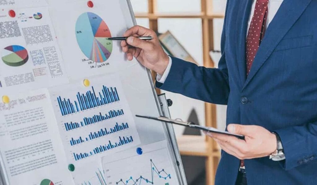 A person in a suit is presenting charts and graphs on a whiteboard, holding a clipboard.